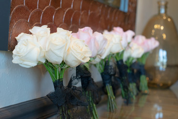 White, pink and yellow roses with stems wrapped in blue lace bows lined up against wall