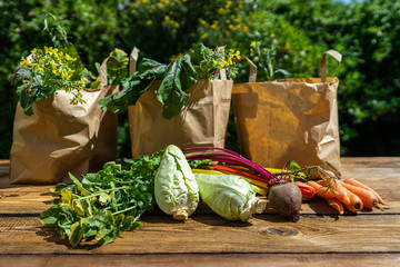 Des légumes sur une table et trois emballages en papier remplis de produits frais
