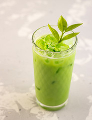 Matcha green tea with milk and ice cubes in a glass of latte on a gray background