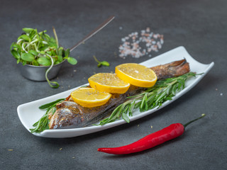 close up view to grilled trout under lemons with pepper and green herbs