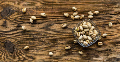 Pistachios in a small plate with scattered nuts of almonds around a plate on a vintage wooden table as a background. Pistachio is a healthy vegetarian protein nutritious food. Natural nuts snacks.