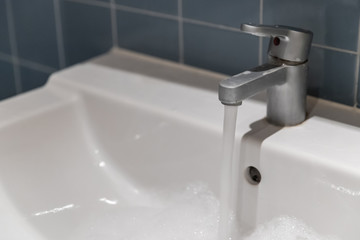 water flowing out of a silver tap at the white sink in bathroom