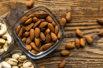 Almonds in a small plate with scattered nuts of almonds around a plate on a vintage wooden table as a background. Almond is a healthy vegetarian protein nutritious food. Natural nuts snacks.