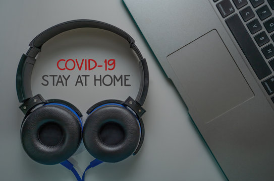 Stay at home advice to stop coronavirus COVID-19 spreading. Global pandemic Covid-19 prevention. Headphone and laptop keyboard on table concept with text "COVID-19 STAY AT HOME"