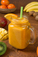 Mango orange banana and kiwi smoothie with ingredients on a brown table. Selected focus.