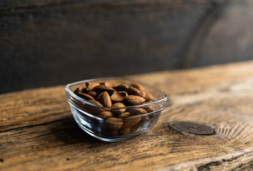 Almonds in a small plate on a vintage wooden table as a background with a copy space. Almond is a healthy vegetarian protein nutritious food. Natural nuts snacks.
