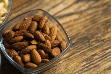 Almonds in a small plate on a vintage wooden table as a background with a copy space. Almond is a healthy vegetarian protein nutritious food. Natural nuts snacks.