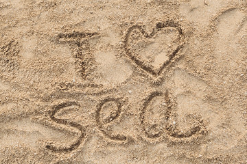 Close-up of «I love sea» phrase handwritten on sand at the seashore at sunrise in summer. Wonderful words on beach sand. Love idea concept