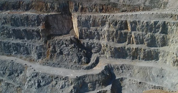 Aerial footage of a steep rock wall at a quarry. It shows mine terraces and landslide
