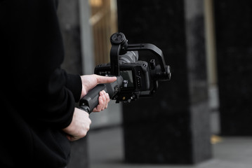 Professional videographer in black hoodie holding professional camera on 3-axis gimbal stabilizer. Filmmaker making a great video with a professional cinema camera. Cinematographer.