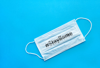 Surgical protective mask on a blue background. Hashtag "Stay home." Blue medical mask for protection against flu, coronavirus and other viruses.