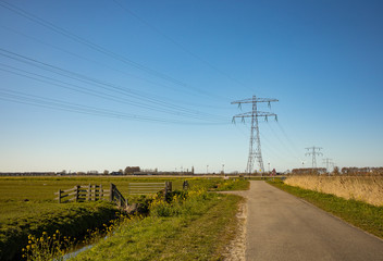 Fototapeta na wymiar High voltage lines and power pylons in a flat and green agricultural landscape on a sunny day with cirrus clouds in the blue sky.