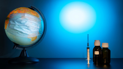 Globe of the earth in a medical mask. World quarantine, coronavirus pandemic. Planet Earth with face mask protect. World medical concept. Blue gradient background. Vials of medicine and a syringe