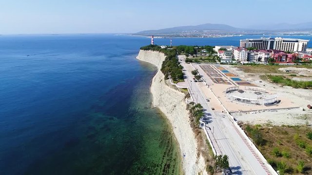 Drone flight over the steep coastline of the Black sea in the region of Gelendzhik. The lighthouse in the background. On the right Bank there are houses and new buildings.