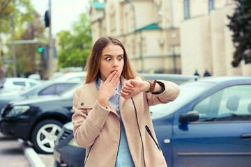Woman being late to a rendez-vous. Closeup portrait headshot view stressed young attractive beautiful businesswoman checking the time outdoor isolated city scape outdoor background near dealership - obrazy, fototapety, plakaty