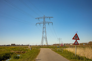 Fototapeta na wymiar High voltage lines and power pylons in a flat and green agricultural landscape on a sunny day with cirrus clouds in the blue sky.