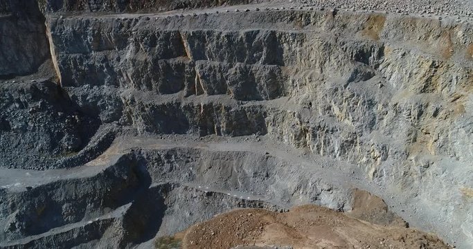 Aerial footage of a steep rock wall at a quarry. It shows mine terraces and landslide