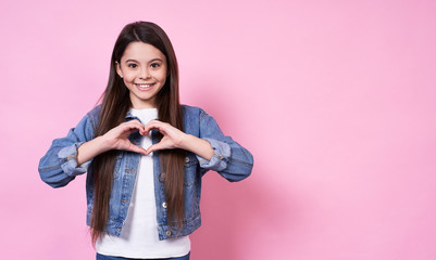 Smiling young girl in a jeans jacket on a pink background.