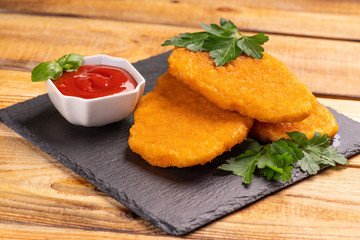 Breaded chicken breasts, schnitzel and ketchup sauce on black burned on wooden background close up.