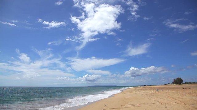 Large beautiful blue sky and white clouds as seen from Kekaha Beach at MacArthur Park on Kauai with a slice of golden sand meeting the gentle white waves rolling to shore.