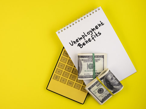 Money In A Wad, A Yellow Calculator, And A White Notebook Marked Unemployment Benefits