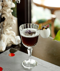 a glass of dark cocktail garnished with egg shell filled with dried flowers
