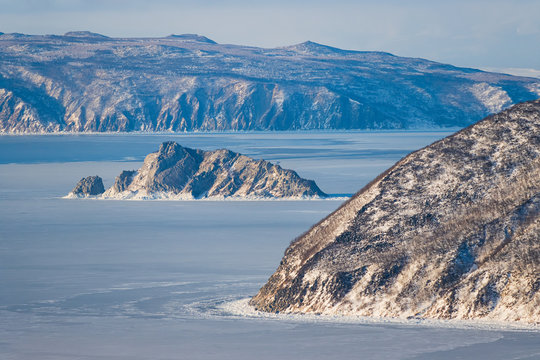 Beautiful view of the sea coast and rocks. Winter landscape with the sea covered with ice. Traveling and Hiking in nature. Coast of the sea of Okhotsk, Magadan Region, Siberia, Far East Russia. - Powered by Adobe