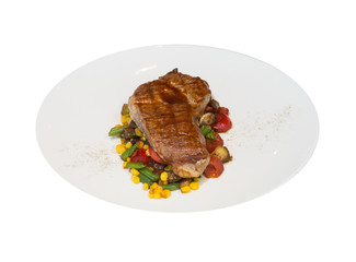 A piece of grilled pork with vegetables on a white plate. Blurred pink background