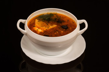 a plate of soup Russian Solyanka with different types of meat on a white plate. against a black reflective surface