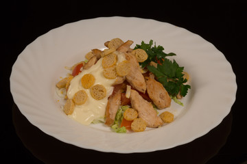 Caesar salad with Turkey, vegetables and breadcrumbs on a white plate. against a black reflective surface