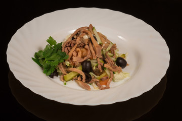 Beef tongue meat salad with vegetables on a white plate. against a black reflective surface