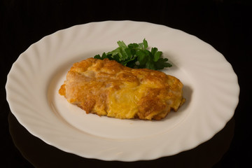 a piece of fish baked in batter with parsley leaves on a white plate