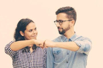 Satisfied couple making fist bump gesture. Young woman in casual and man in glasses standing isolated over white background. Cooperation concept