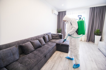 Disinfector in a protective suit conducts disinfection in contaminated area of house to prevent...