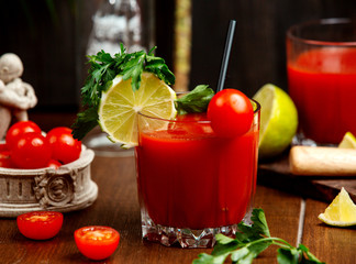 a glass of tomato juice garnished with cherry tomato lemon and parsley