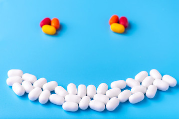 White and colored pills lie in the form of a smile on a blue background. Close-up, top view, macro photography. Lots of white mints.