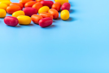 Obraz premium Multi-colored shiny dragees with fillings of orange, wild berries, lemon are scattered on a blue background. The view from the top.