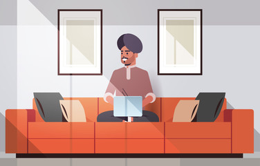 indian man in turban sitting on couch using laptop guy working from home freelance concept modern living room interior horizontal full length vector illustration