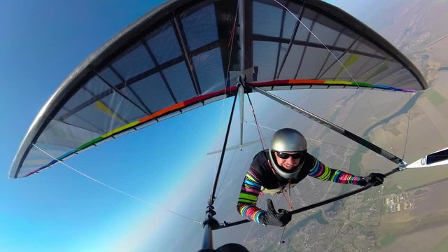 Smiling hang glider pilot shows thumb up while flyingh high above ground on his colorful wing