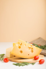 Various types of cheese with rosemary and tomatoes on wooden board on a white and orange background. Side view, copy space.