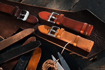Brown leather handmade watch straps with metal buckles laying on the brown leather cutting near to...