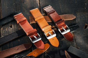 Fototapeta na wymiar Leather brown watch straps with steel buckles laying on the dark wooden surface. 