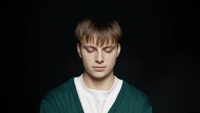 Close up of young man looking up at camera. Young man in casuals on black background.
