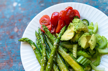 White plate with asparagus, avocado, celery and cherry tomatoes