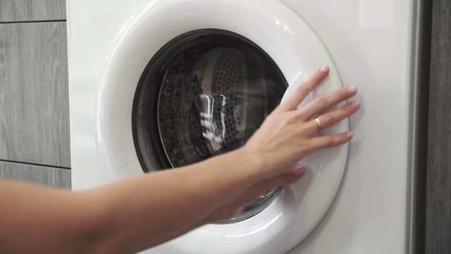 Female hand with married ring puts PURPLE CLOTHES in laundry machine. Loading washing machine. Load clothes to washer machine. Load clothes laundry washing machine. Preparing laundry washing