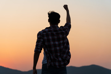 Man with fist in the air during sunset sunrise mountain in background. Stand strong. Feeling...