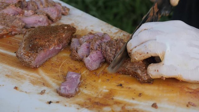 Close up on hands holding a smoked brisket on a cutting board and quickly slicing cooked beef meat into thin slices for a barbecue.