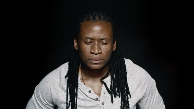 African man with his eyes closed. Close up of a male with dreadlocks on black background
