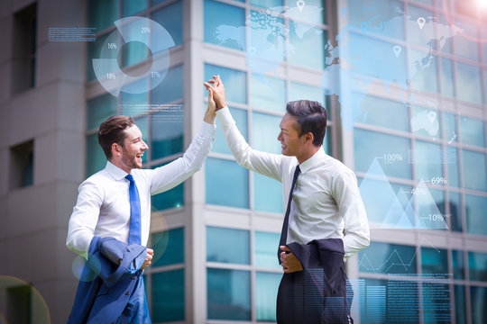 Two Businessmen High Fiving And Virtual Statistic Graphics. Closeup Of Two Smiling Business Men In Front Of Office Building At Background. Side View.