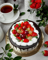 top view of chocolate dripping cake topped with strawberry and grapes